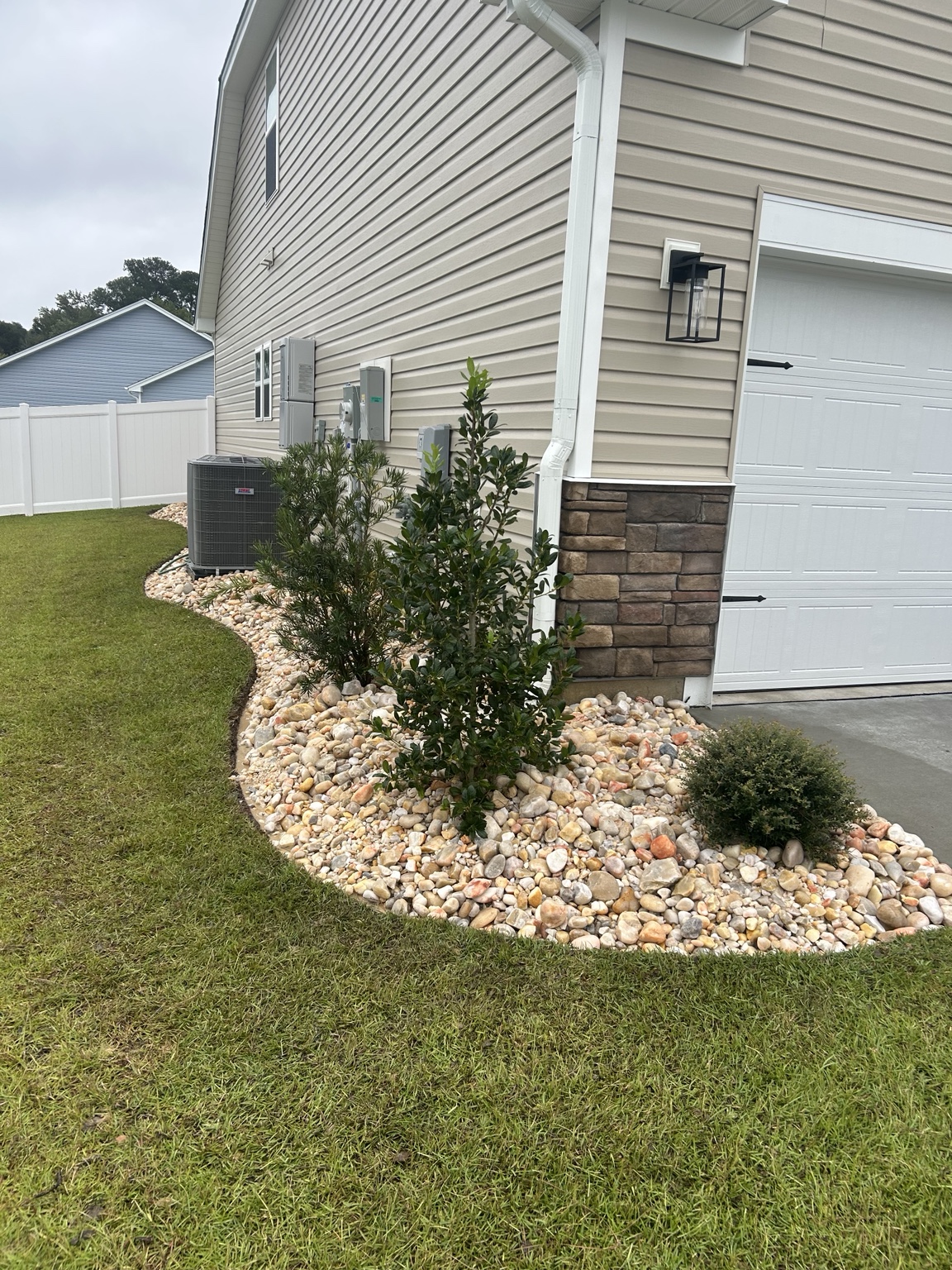 Curved 2 to 5 inch Carolina River Rock landscape bed beside a home garage